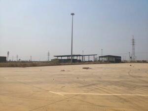 Área pavimentada no Polo Industrial de Viana, com estruturas e postes ao fundo.