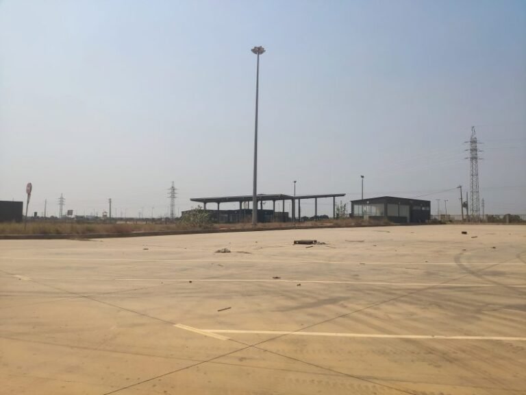 Área pavimentada no Polo Industrial de Viana, com estruturas e postes ao fundo.