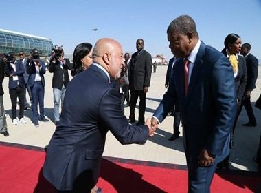 Dois homens de fato cumprimentam-se junto a uma passadeira vermelha.
