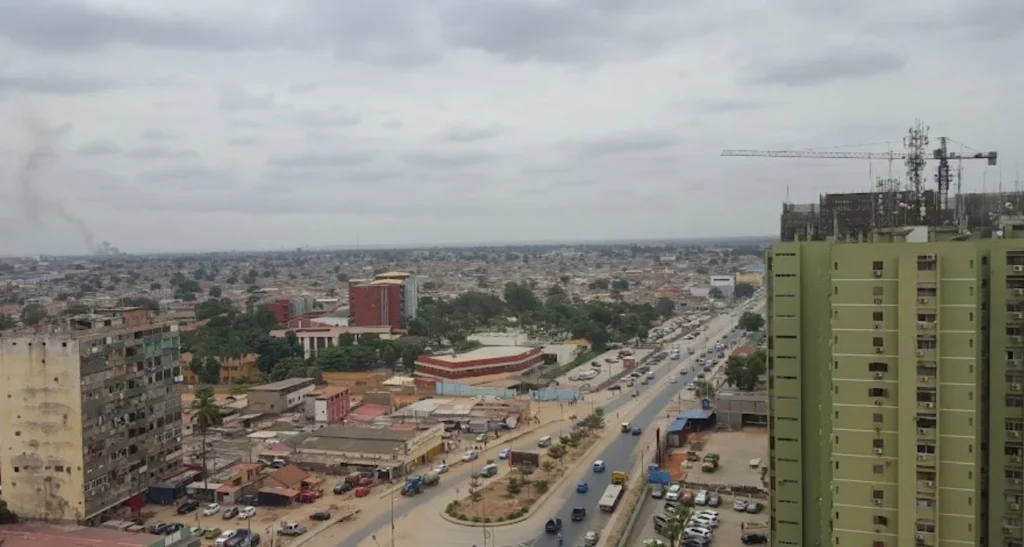 Vista urbana do Rangel, em Luanda, com edifícios, uma avenida movimentada e uma grua de construção.