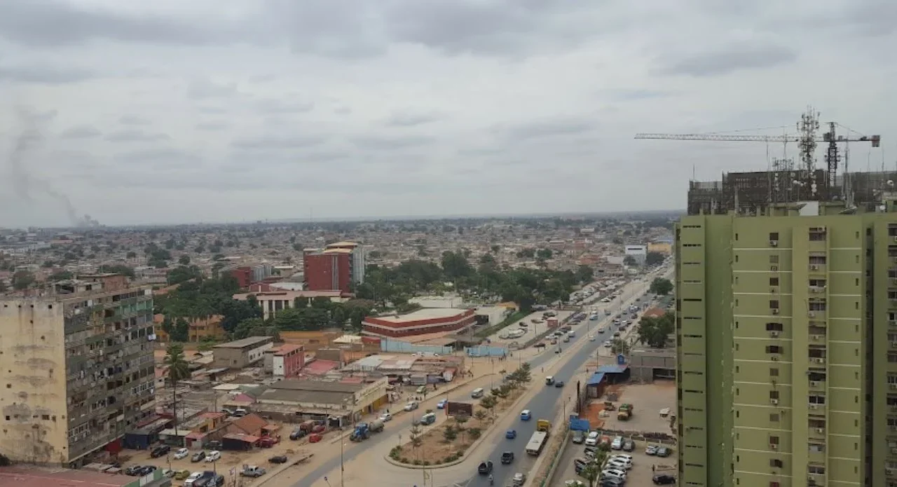 Vista urbana do Rangel, em Luanda, com edifícios, uma avenida movimentada e uma grua de construção.