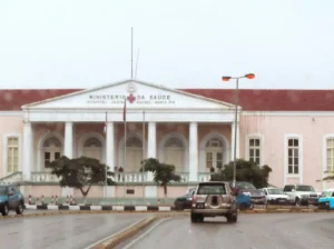 Fachada do Hospital Josina Machel, com colunas brancas, árvores e viaturas na rua em frente.
